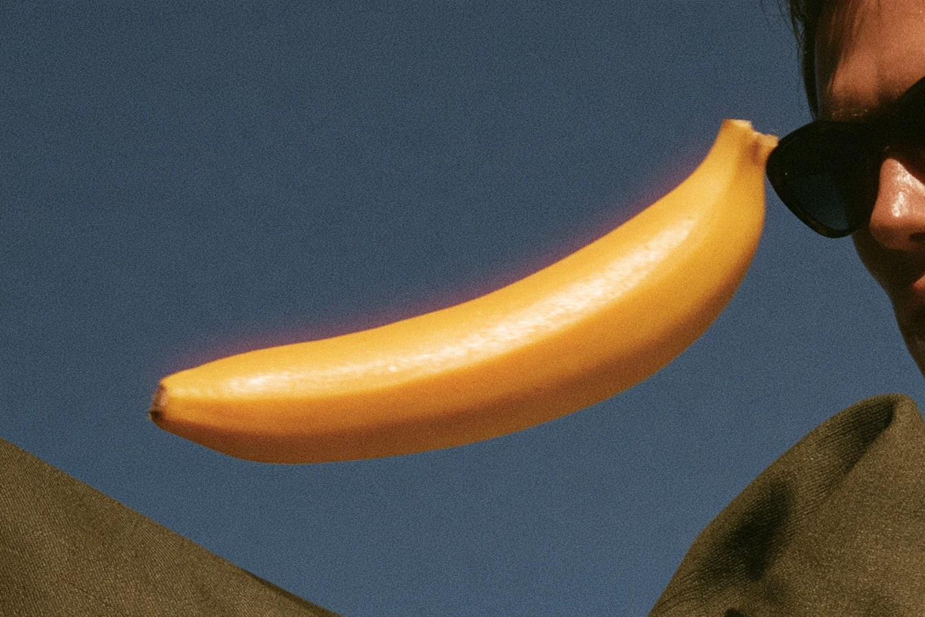 Banana held against a blue sky with a red-orange glow along its bright edge