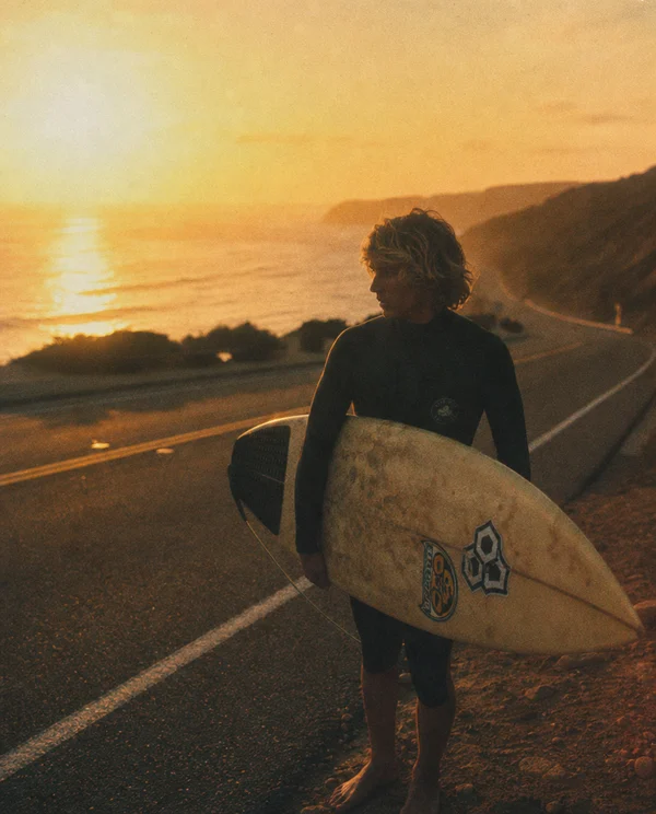Surfer Standing on a Coastal Road at Sunset