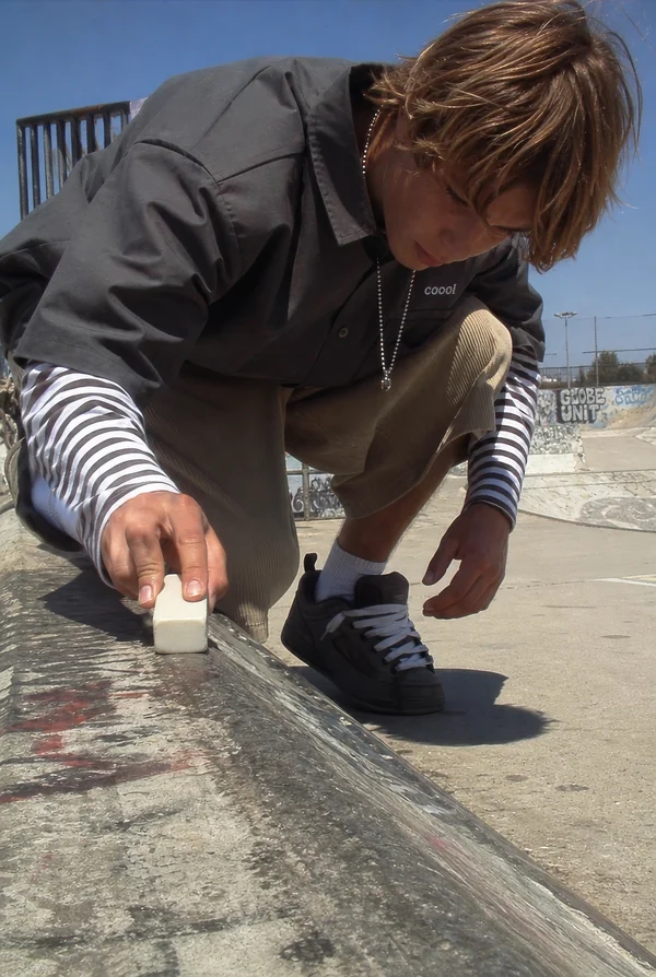 Skater waxing a concrete ledge at a skatepark