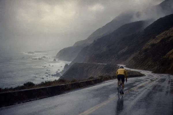 Cyclist Riding Along a Misty Coastal Highway