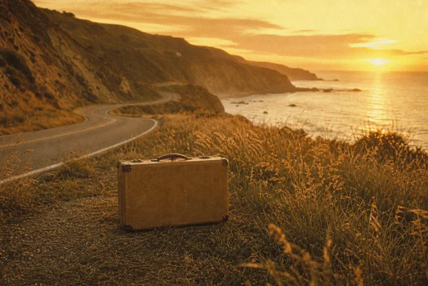 A Vintage Suitcase on a Coastal Road at Sunset