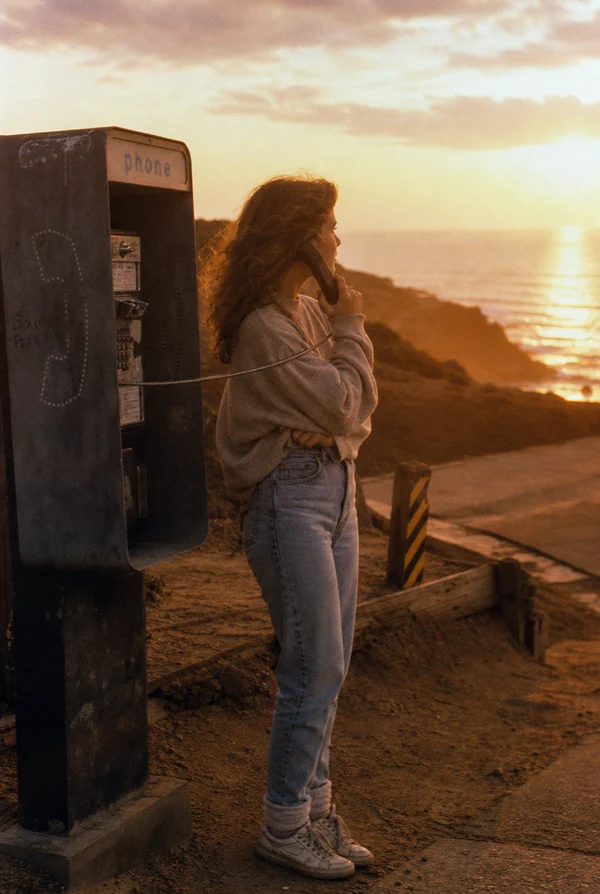 Woman Using a Payphone at Sunset by the Ocean